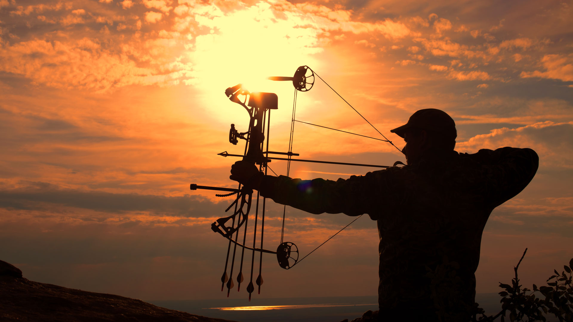 A camo-clad bowhunter drawing a compound bow against a blazing sunset — the stillness and one-shot focus that carry over to the river